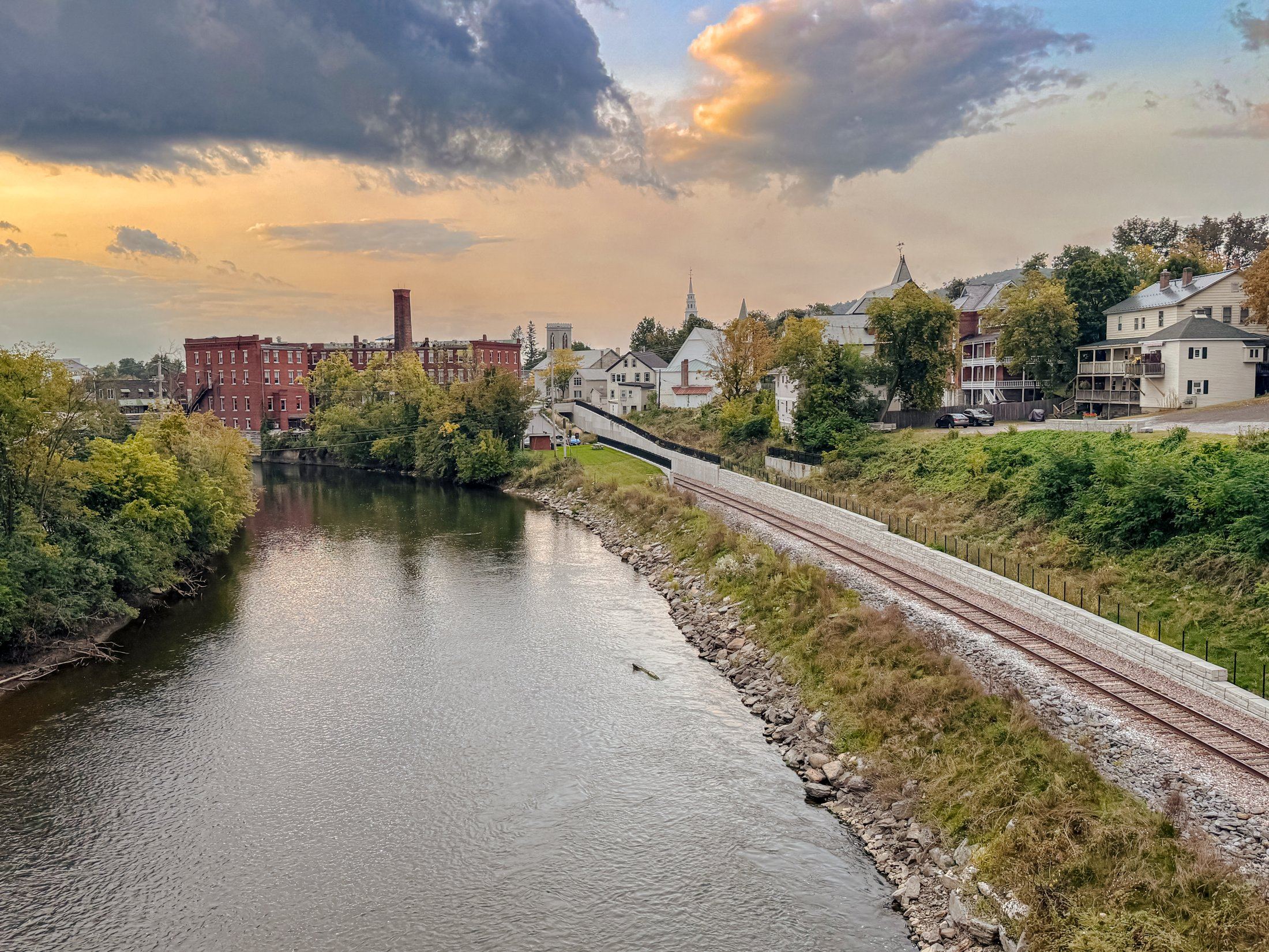 A small town in cross-section: river, rail line, mill buildings, steeples, and houses on the hill