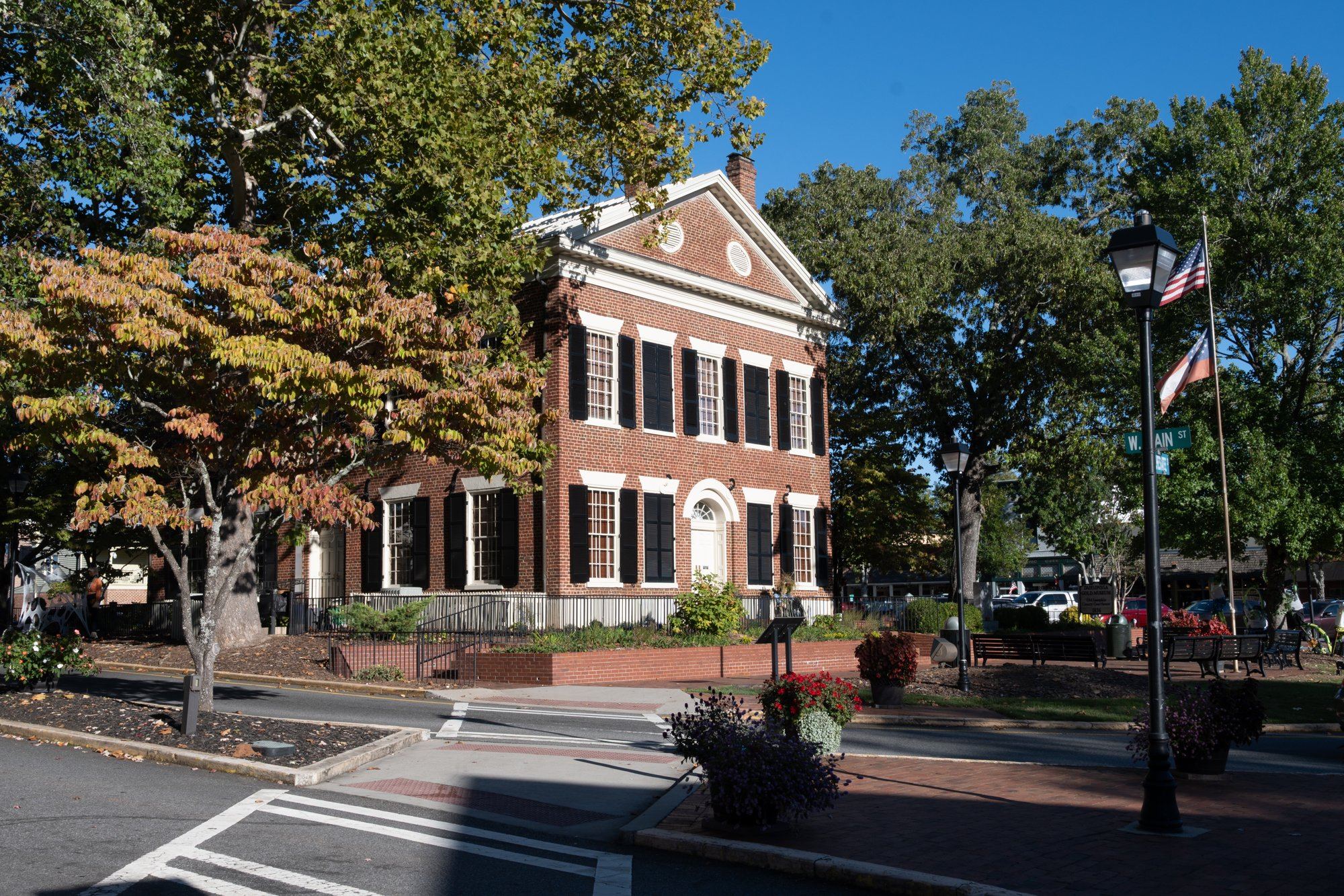 A brick courthouse on a tree-lined town square, with flags and a street lamp