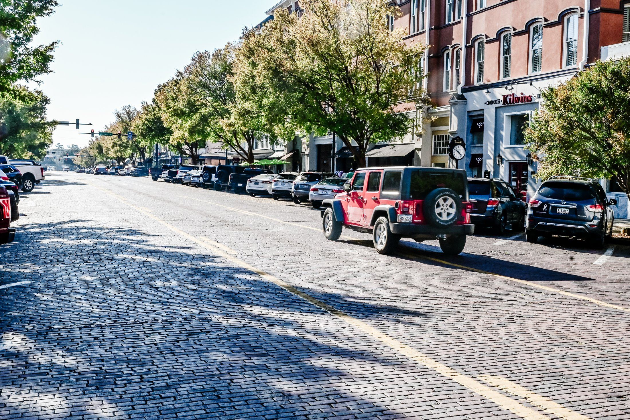 A small-town main street at eye level: brick storefronts, string lights, and a street clock